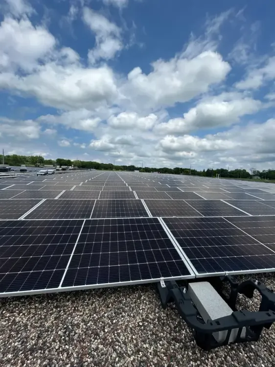 Field of solar panels all the way to the horizon, under a blue sky with puffy clouds.