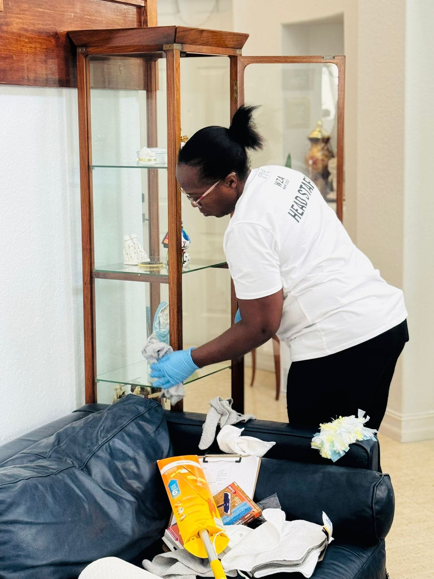 A woman cleaning a tall glass antique case with a cleaning cloth