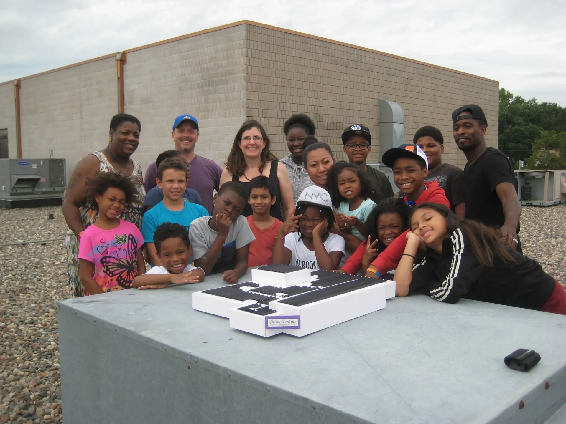 A group of 20 people, ranging from toddlers to adults, posing at a white table outdoors