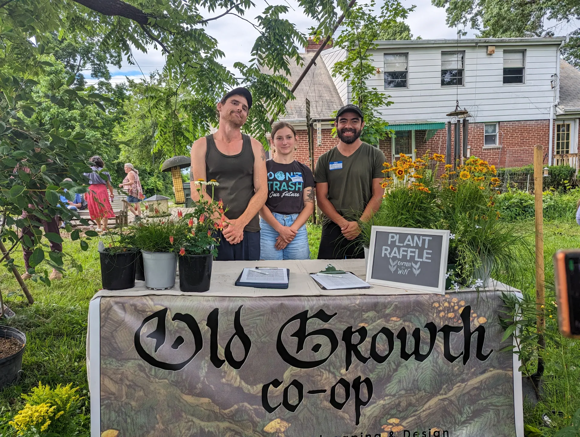 3 members of the Old Growth team standing at a table surrounded by beautiful plants