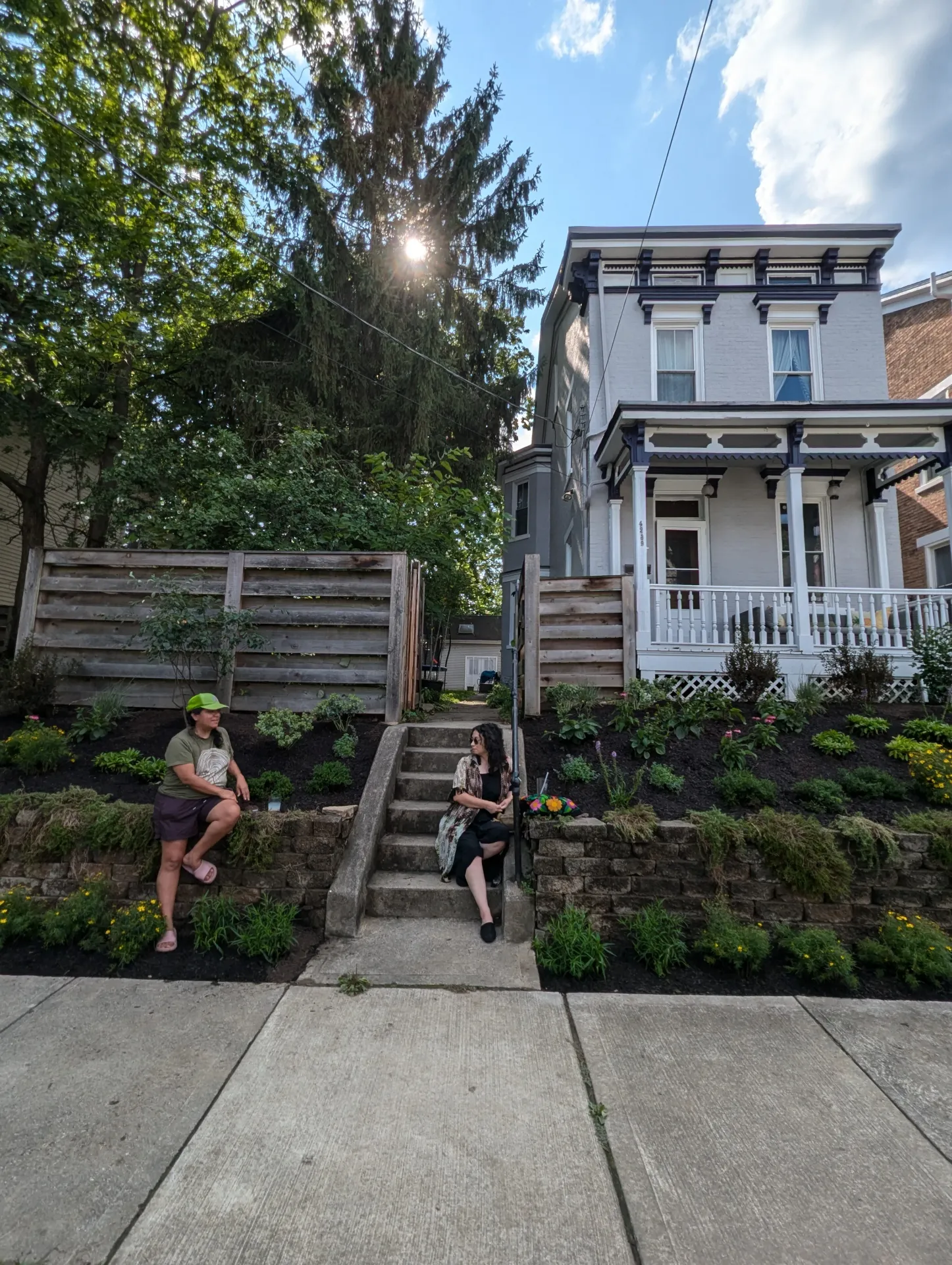 A blue two-story house with a beautiful front yard full of well-manicured plants