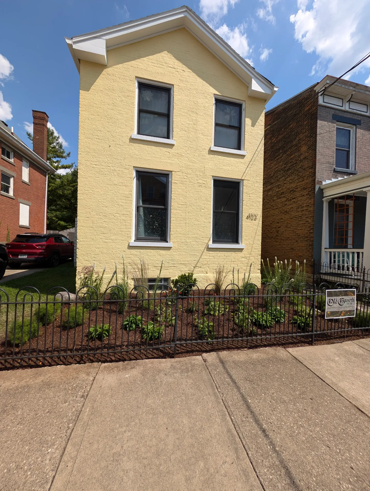 A 2-story house next to a sidewalk with a beautifully manicured garden